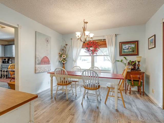 dining space with a textured ceiling, an inviting chandelier, and light hardwood / wood-style floors