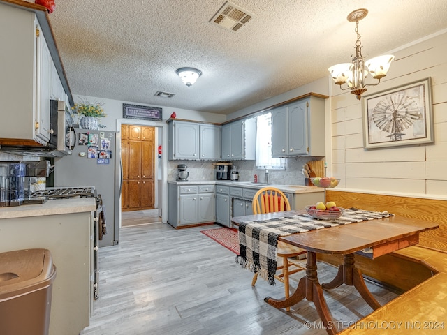 kitchen with light wood-type flooring, gray cabinets, a notable chandelier, a textured ceiling, and white range with gas stovetop