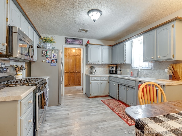 kitchen with a textured ceiling, appliances with stainless steel finishes, light hardwood / wood-style floors, sink, and gray cabinets