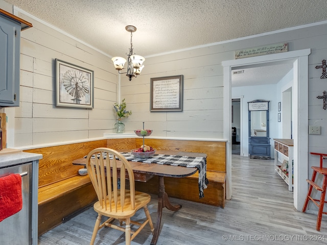 dining area with wooden walls, crown molding, hardwood / wood-style floors, a notable chandelier, and a textured ceiling