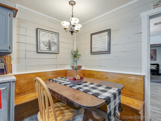 dining space with hardwood / wood-style flooring, wooden walls, crown molding, and a textured ceiling