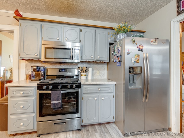 kitchen featuring gray cabinets, a textured ceiling, tasteful backsplash, stainless steel appliances, and light hardwood / wood-style floors