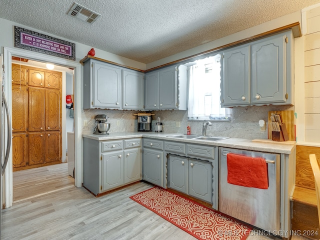 kitchen with a textured ceiling, dishwasher, sink, and light hardwood / wood-style floors