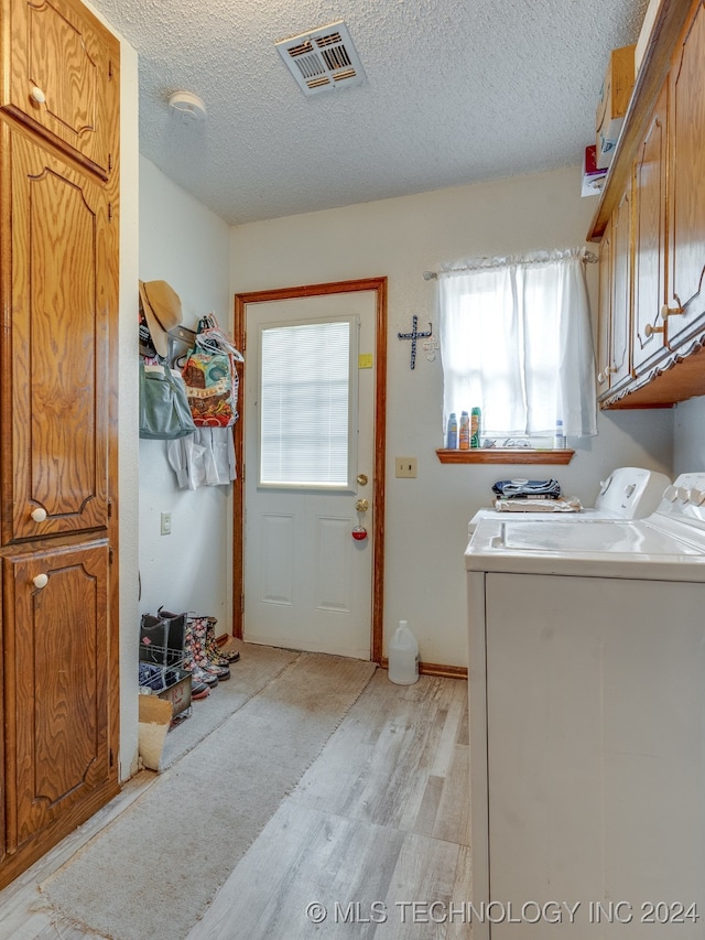 laundry room featuring a textured ceiling, cabinets, independent washer and dryer, and light wood-type flooring