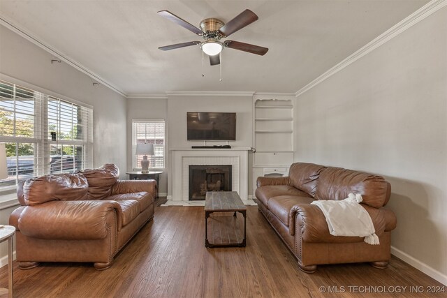 living room with dark wood-type flooring, ceiling fan, ornamental molding, and a fireplace