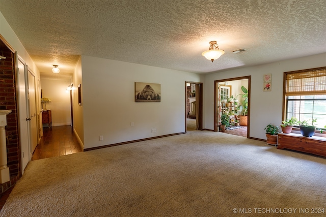 unfurnished room with a textured ceiling, light colored carpet, and a fireplace