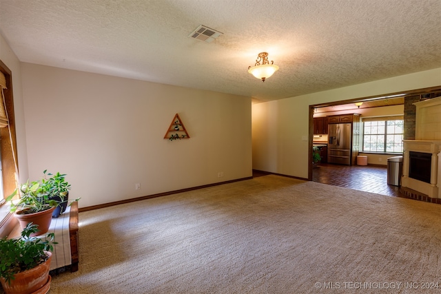 unfurnished living room featuring dark carpet, a large fireplace, and a textured ceiling