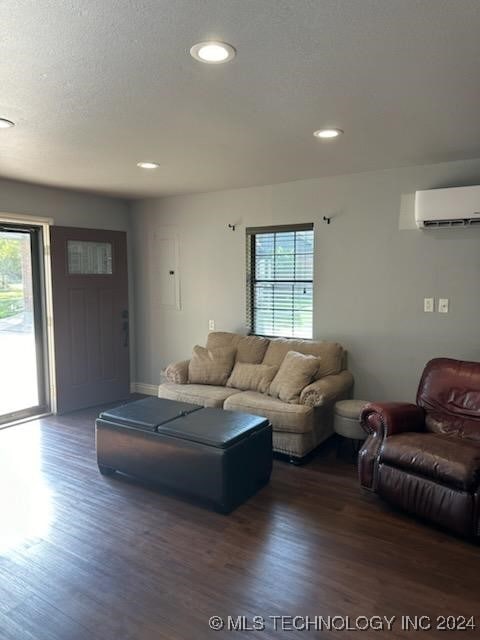 living room featuring a textured ceiling, dark hardwood / wood-style floors, a wall unit AC, and a wealth of natural light