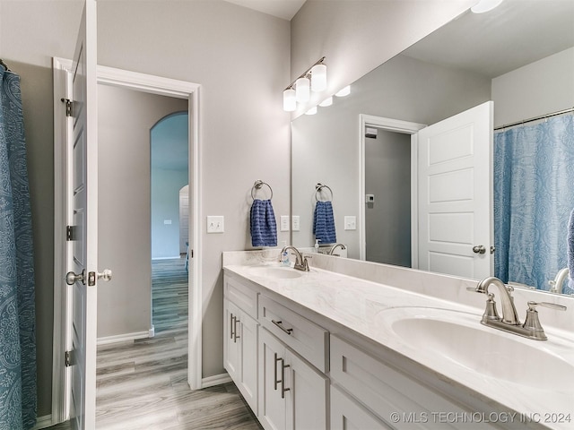 bathroom with double vanity, wood finished floors, a sink, and baseboards