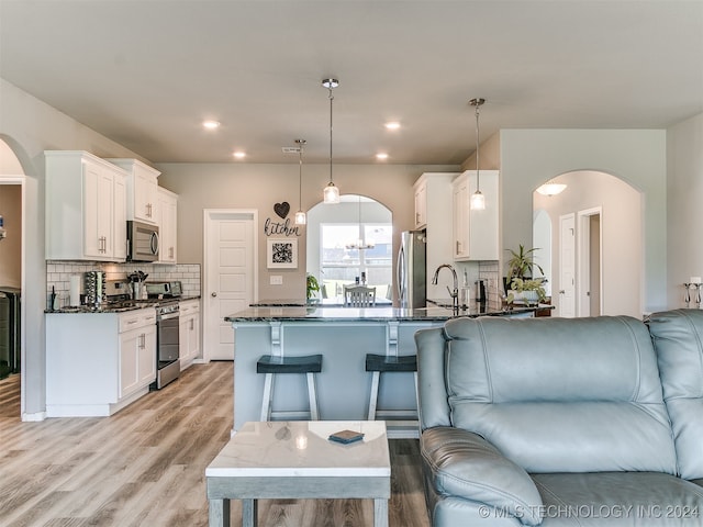 kitchen featuring hanging light fixtures, dark stone countertops, light hardwood / wood-style flooring, stainless steel appliances, and kitchen peninsula