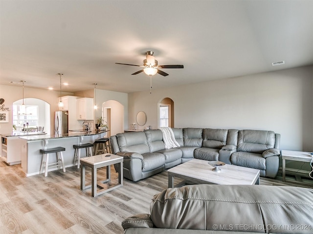 living room featuring light wood-type flooring, arched walkways, visible vents, and a ceiling fan