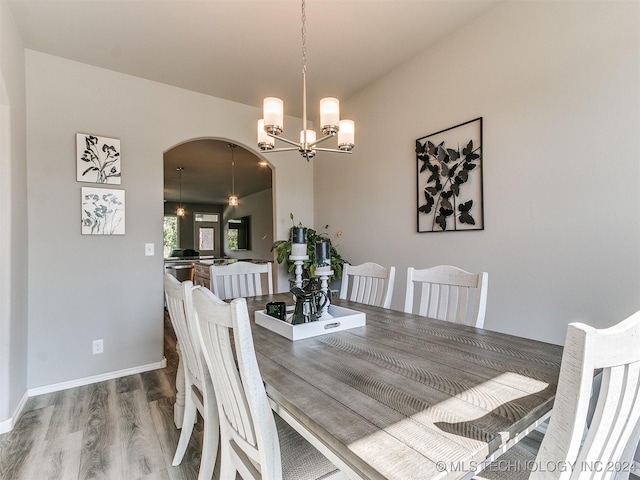 dining space with arched walkways, baseboards, an inviting chandelier, and wood finished floors