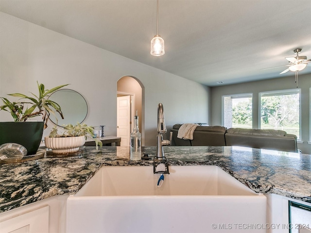 kitchen featuring arched walkways, hanging light fixtures, open floor plan, a sink, and dark stone countertops