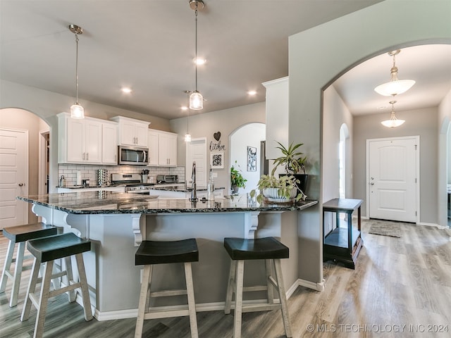 kitchen with decorative light fixtures, light hardwood / wood-style flooring, stainless steel appliances, decorative backsplash, and white cabinetry