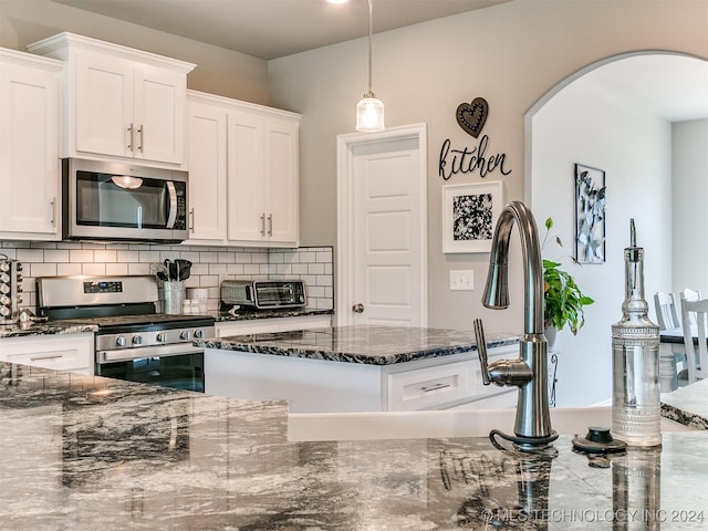 kitchen featuring tasteful backsplash, dark stone counters, hanging light fixtures, stainless steel appliances, and white cabinetry