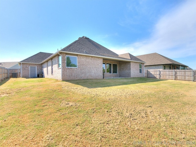 back of property with brick siding, a fenced backyard, cooling unit, and a yard