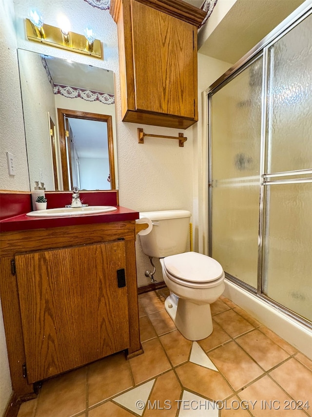 bathroom with vanity, a shower with shower door, toilet, and tile patterned flooring