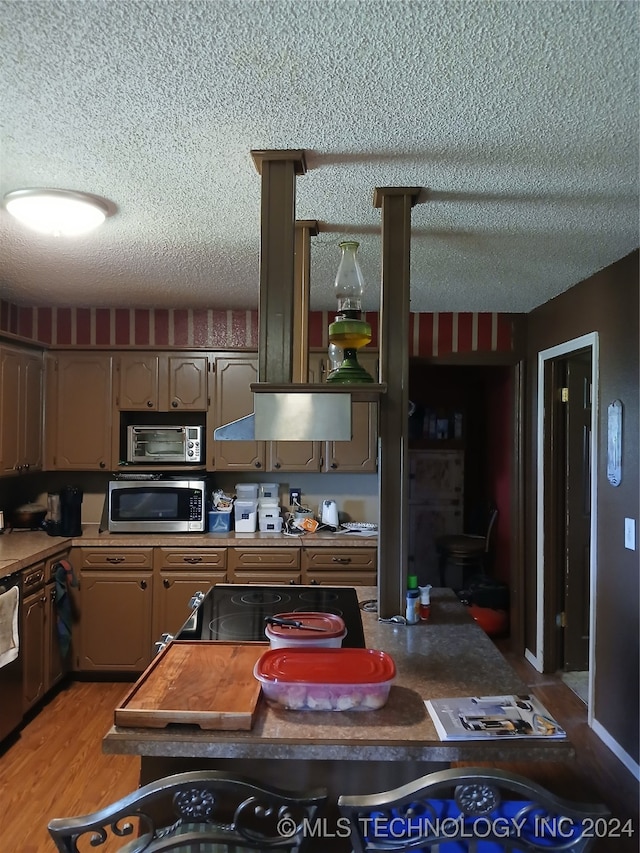 kitchen with light wood-type flooring, dishwashing machine, and a textured ceiling