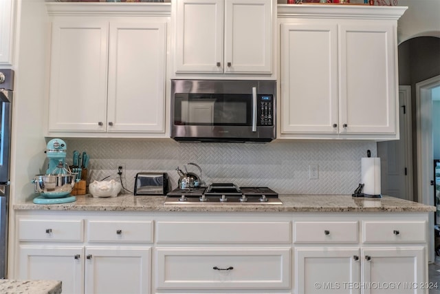 kitchen with stainless steel appliances, backsplash, white cabinets, and light stone counters