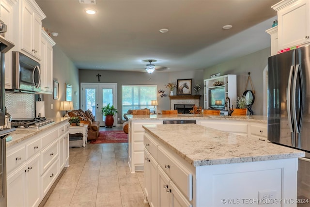 kitchen with a center island, kitchen peninsula, stainless steel appliances, light stone countertops, and french doors