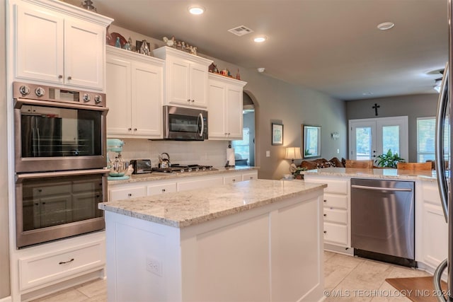 kitchen with backsplash, stainless steel appliances, a center island, light stone countertops, and white cabinets