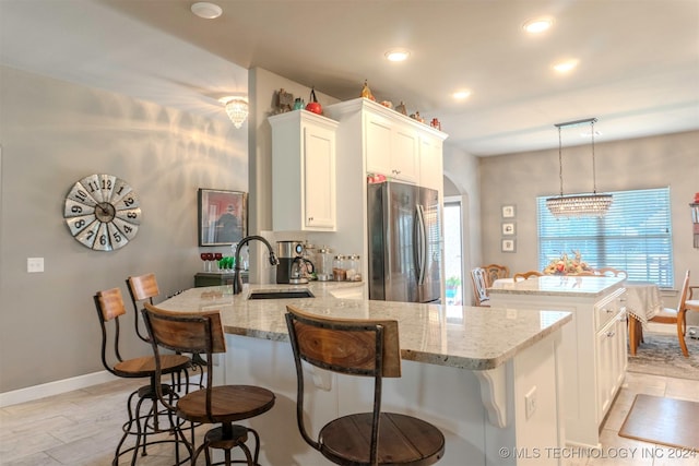 kitchen featuring sink, stainless steel fridge, hanging light fixtures, white cabinets, and a kitchen island