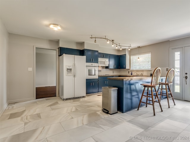 kitchen with blue cabinetry, kitchen peninsula, a breakfast bar, and white appliances