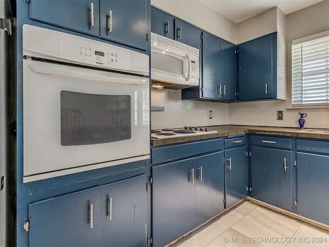 kitchen featuring light tile patterned flooring, white appliances, and blue cabinetry