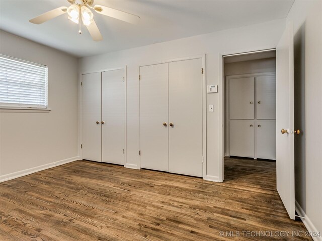 unfurnished bedroom featuring ceiling fan, wood-type flooring, and two closets