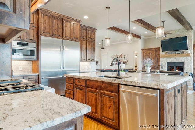 kitchen with light wood-type flooring, light stone countertops, stainless steel appliances, and a center island with sink