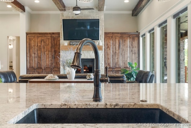 kitchen featuring light stone counters, ornamental molding, sink, and a stone fireplace