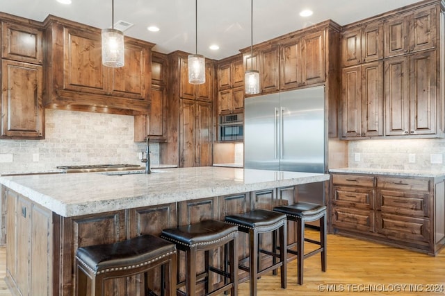 kitchen featuring pendant lighting, light stone counters, a center island with sink, and light hardwood / wood-style flooring