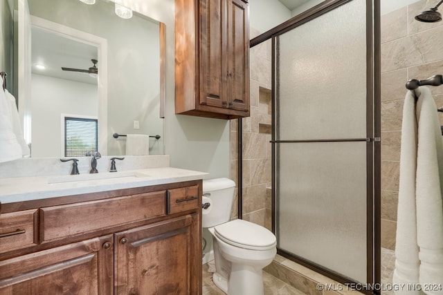 bathroom featuring a shower with shower door, toilet, vanity, and ceiling fan