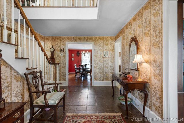 entrance foyer featuring dark tile patterned floors, a chandelier, and crown molding