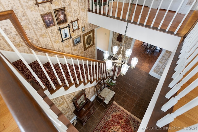 staircase with wood-type flooring, a towering ceiling, and an inviting chandelier