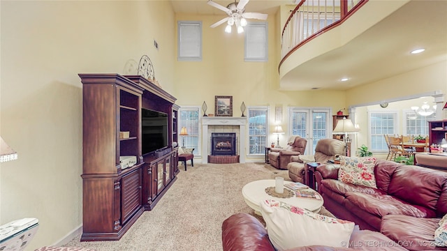 living room featuring carpet, ceiling fan with notable chandelier, a high ceiling, and a fireplace