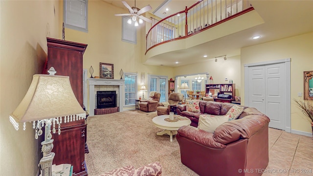 living room with a tiled fireplace, a towering ceiling, light tile patterned floors, and ceiling fan