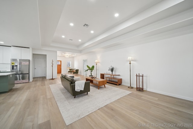 living room featuring a tray ceiling, light wood-type flooring, and a notable chandelier