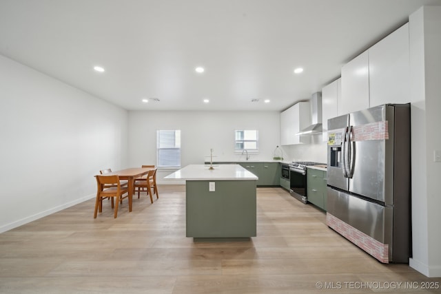 kitchen with appliances with stainless steel finishes, a kitchen island with sink, wall chimney range hood, and white cabinets