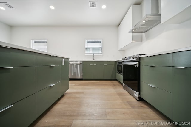 kitchen featuring a wealth of natural light, stainless steel appliances, wall chimney range hood, and green cabinetry