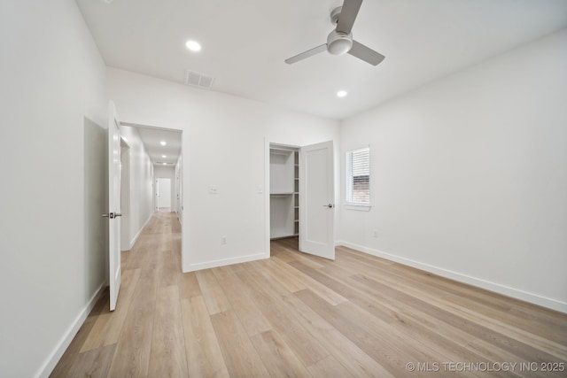 unfurnished bedroom with ceiling fan, a spacious closet, a closet, and light wood-type flooring