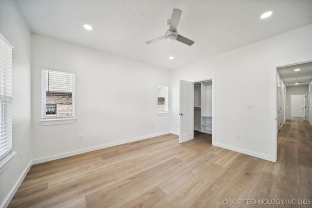 unfurnished bedroom with a spacious closet, light wood-type flooring, ceiling fan, and a closet