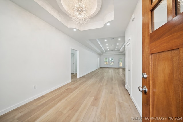 interior space with a chandelier, light wood-type flooring, and a tray ceiling