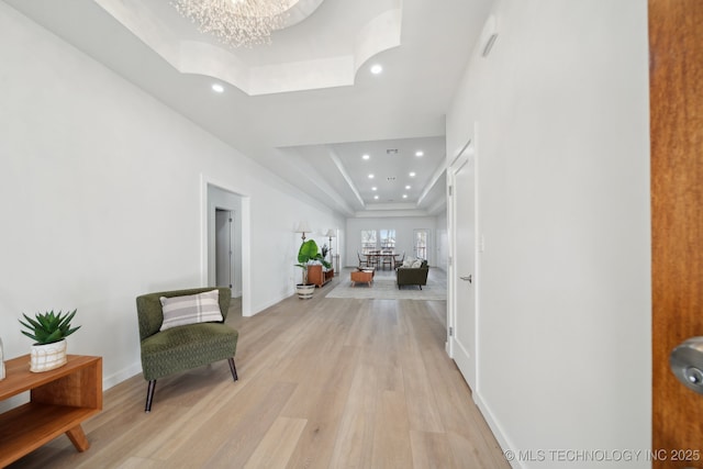 hall featuring an inviting chandelier, a tray ceiling, and light hardwood / wood-style flooring