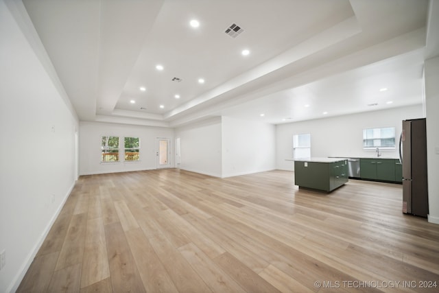 unfurnished living room featuring a tray ceiling, sink, a healthy amount of sunlight, and light wood-type flooring