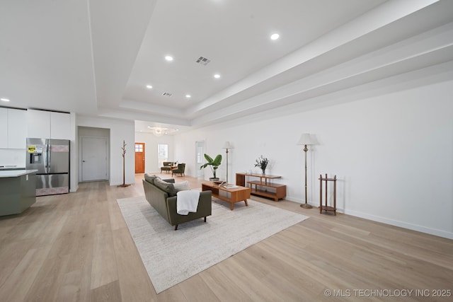 living room featuring a tray ceiling, a chandelier, and light wood-type flooring