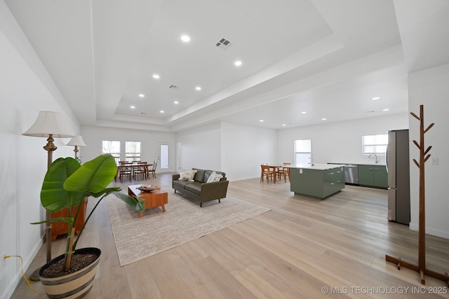 living room with plenty of natural light, sink, light hardwood / wood-style flooring, and a tray ceiling