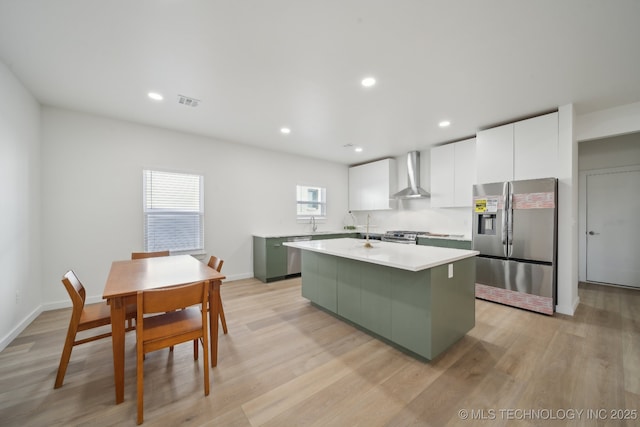 kitchen with stainless steel appliances, a kitchen island with sink, wall chimney range hood, and white cabinets