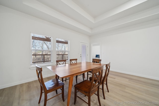 dining space with light wood-type flooring and a tray ceiling