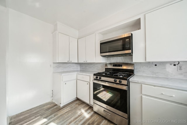 kitchen with white cabinets, appliances with stainless steel finishes, light hardwood / wood-style floors, and decorative backsplash